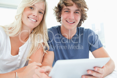 A smiling couple holding a tablet and looking at the camera