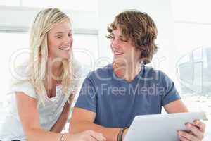 A smiling couple holding a tablet and looking at each other