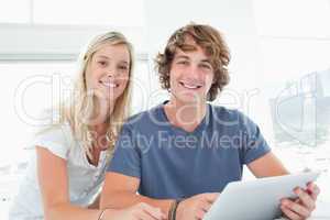 A smiling couple holding a tablet and looking at the camera