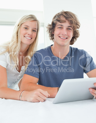Close up smiling couple holding a tablet and looking at the came