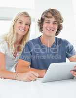 Close up smiling couple holding a tablet and looking at the came
