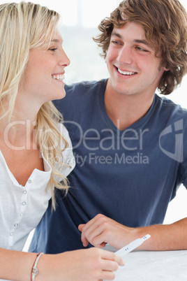 A smiling couple looking at one another as they hold a pregnancy