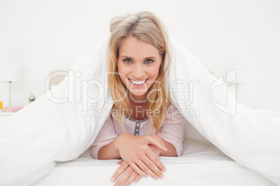 Woman at end of the bed, under a quilt smiling and looking forwa
