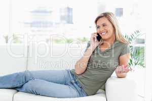 Woman smiling as she lies across the couch, making a call with a