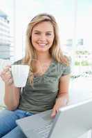 Woman looking forward with a cup in her hand, as she uses her la