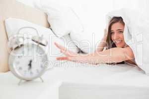 Woman under the quilt reaches out to try and silence her alarm c