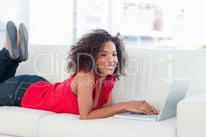 Woman with raised legs on the couch smiling and using her laptop
