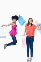 A teenage girl jumping with her shopping bags while her friend i