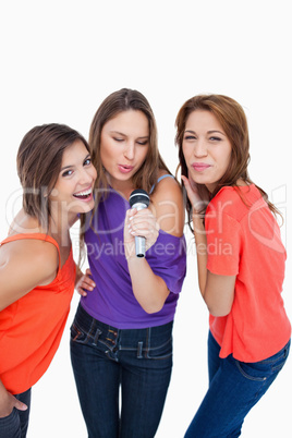Three attractive young women singing in a microphone