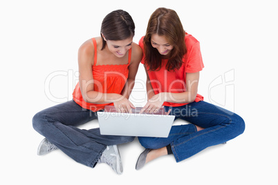 Two cute teenagers sitting cross-legged while looking at a lapto