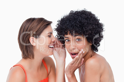 Teenage girl whispering a secret to a surprised friend