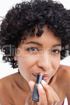 Young woman looking at the camera while applying lipstick