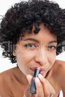 Young woman looking at the camera while applying lipstick