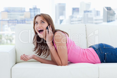 Teenage girl enjoying her phone call while lying on a white sofa