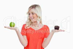 Young woman holding an apple and a muffin while looking at the a