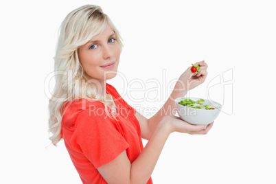 Side view of a young blonde woman eating vegetable salad