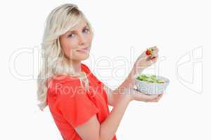 Side view of a young blonde woman eating vegetable salad