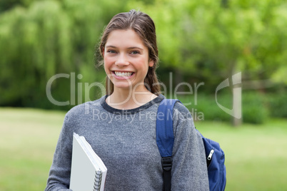 Young happy adult coming back from school while holding a notebo