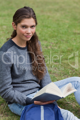 Calm student holding a book while sitting next to her backpack