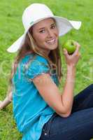 Attractive young woman sitting down while eating an apple