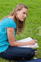 Attractive young girl sitting down in a park while doing her hom