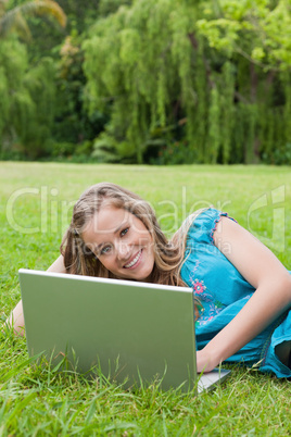 Young smiling girl using her laptop while lying on the grass