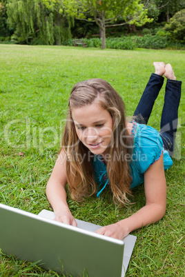 Young girl lying on the grass while raising her legs and using h