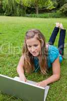 Young girl lying on the grass while raising her legs and using h