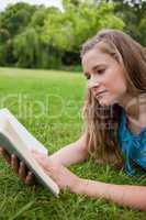 Serious young woman reading a book while lying on the grass