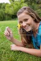 Young smiling girl smelling a yellow flower while lying on the g