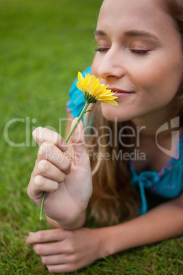 Young relaxed girl smelling a flower while lying on the grass