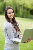 Young smiling woman holding her laptop while standing upright in