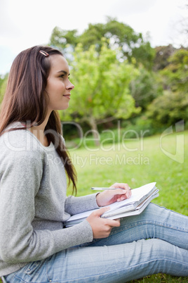 Young relaxed girl looking far away while holding her pen and he