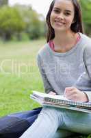 Smiling student doing her homework while sitting on the grass