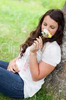 Young pretty woman leaning against a tree while smelling flowers