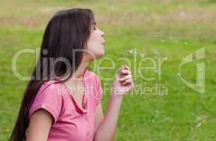 Young woman standing up in a park while blowing a dandelion