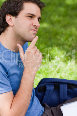 Young man placing his finger on his chin while sitting in a park