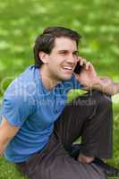 Young man laughing while sitting on the grass and talking on the