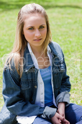 Young serious girl sitting on the grass while looking at the cam