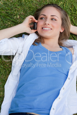 Young smiling girl lying on her back on the grass while calling