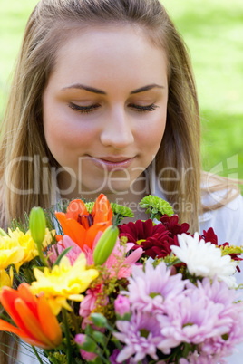 Young peaceful woman smelling a bunch of flowers while closing h