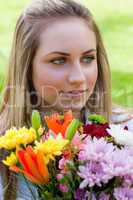 Young relaxed blonde girl holding a bunch of flowers while looki