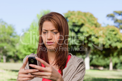 Serious woman reading a text message in a bright grassland area