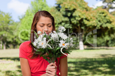 Woman smelling a bunch of flowers while standing in a park