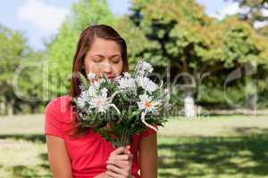 Woman smelling a bunch of flowers while standing in a park