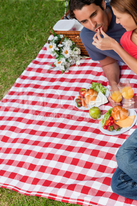 Woman putting food into her friends mouth as they lie on a blank