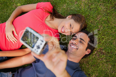 Man taking a photo with his friend while lying side by side