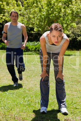 Woman bending over while a man is jogging in the background