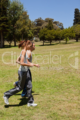 Two friends jogging along side each other across grass
