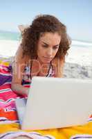 Young woman lying on her beach towel while using a laptop